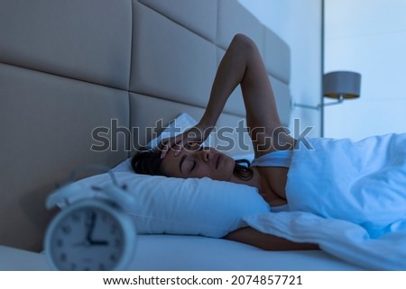 Sleepless and desperate beautiful woman awake at night not able to sleep looking at clock suffering from insomnia in sleep disorder concept. Woman suffering from insomnia. Blue night time effect 