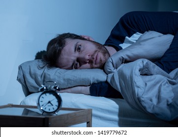 Sleepless and desperate young caucasian man awake at night not able to sleep, feeling frustrated and worried looking at clock suffering from insomnia in stress and sleeping disorder concept. - Shutterstock ID 1419779672