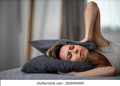 Sleepless lady covering ears with pillow. Noisy neighbors, tinnitus, insomnia or stress concept. Tired woman can't sleep. Awake in bed after coming home from her shift, work.