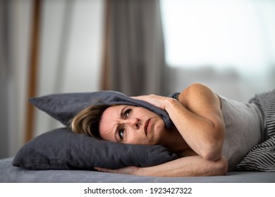 Sleepless Lady Covering Ears With Pillow. Noisy Neighbors, Tinnitus, Insomnia Or Stress Concept. Tired Woman Can't Sleep. Awake In Bed After Coming Home From Her Shift, Work.