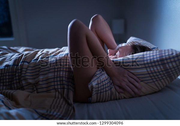 Sleepless lady covering ears with pillow. Noisy\
neighbors, tinnitus, insomnia or stress concept. Tired woman can\'t\
sleep. Awake in bed in the middle of the night. Noise from party\
next door.