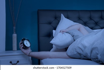 a sleepless man hold his pillow and alarm clock at night - Shutterstock ID 1704527509