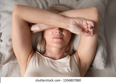 Sleepless mature woman suffering from insomnia close up, lying in bed, older female covering eyes with hands, trying to sleep, nightmares or depression, feeling headache or migraine - Powered by Shutterstock