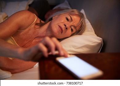 Sleepless Senior Woman In Bed At Night Checking Mobile Phone