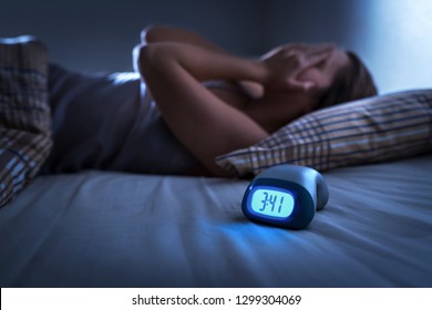 Sleepless woman suffering from insomnia, sleep apnea or stress. Tired and exhausted lady. Headache or migraine. Awake in the middle of the night. Frustrated person with problem. Alarm clock with time.