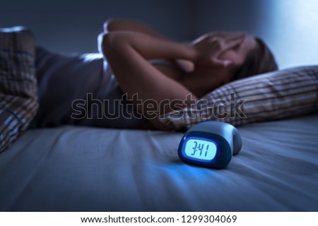 Sleepless woman suffering from insomnia, sleep apnea or stress. Tired and exhausted lady. Headache or migraine. Awake in the middle of the night. Frustrated person with problem. Alarm clock with time.
