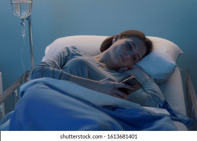 Sleepless worried patient lying in bed late at night at the hospital and chatting with her smartphone - Powered by Shutterstock