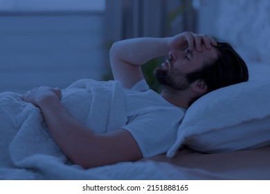 Sleepless Young Man Laying In Bed Alone At Night, Touching His Head, Having Heavy Thoughts Or Suffering From Migraine, Side View, Copy Space. Depression, Insomnia, Apathy Concept