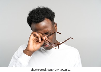Sleepy African American man take off glasses rubbing his eyes feels tired after work on laptop computer isolated on grey background. Exhausted black male wants to sleep. Overwork, chronic fatigue eyes