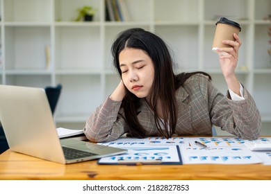 Sleepy Asian Businesswoman Yawning At Work In The Afternoon After Being Tired And Fed Up With Working With Laptop And Financial Graph Documents At Work.