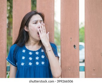 Sleepy Asian Woman With Yawn Motion On Blurred Wooden Fence Background