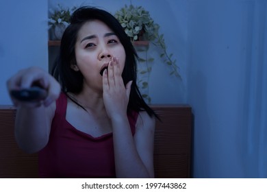 schlampige Asiatin-Frau, die im Bett mit der Hand gähnelt, die fernfernfernfernfernsehmüde vom Anschauen von Serien, Filme im Fernsehen spät nachts mit dunklen Augenkreisen