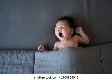 sleepy baby yawning. naked asian baby infant sleeping on gray bed with blanket. studio shot. 