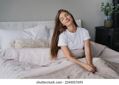 Sleepy blonde caucasian young woman in white t-shirt sitting on bed eyes closed awakening cute smiling at Sunday morning. Relaxed Italian girl with long loose hair enjoys weekend at cozy home. - Shutterstock ID 2245057695