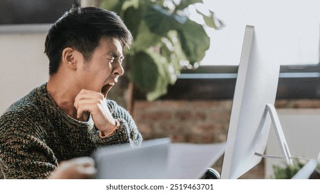 Sleepy businessman yawning in the office. Asian man looking tired in front of a computer. Asian office worker tired and sleepy by computer. Asian businessman yawning of exhaustion. - Powered by Shutterstock