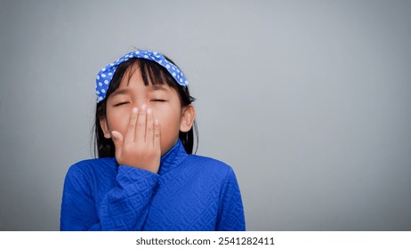 Sleepy child girl yawning while covering her mouth isolated on grey background - Powered by Shutterstock