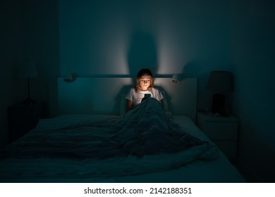 Sleepy exhausted woman lying in bed using smartphone, can not sleep. Insomnia, addiction concept. Sad girl bored in bed scrolling through social networks on mobile phone late at night in dark bedroom. - Shutterstock ID 2142188351