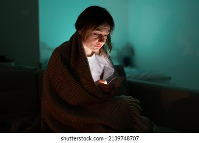 Sleepy Exhausted Woman Sitting On Sofa Using Smartphone, Can Not Sleep. Insomnia, Addiction. Sad Girl Bored In Bed Scrolling Through Social Networks On Mobile Phone Late At Night In Dark Bedroom.