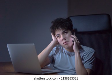 Sleepy Exhausted Young Asian Man Working Late Night At Office Desk With His Laptop, He Is Boring And Not Happy With His Work, Sleep Deprivation And Overtime Overload Working Concept.