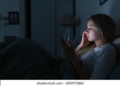 Sleepy Exhausted Young Woman Lying In Bed Using Smart Phone, Chatting And Bored, Can Not Sleep. Insomnia, Nomophobia, Sleep Disorder Concept. Social Media Addiction