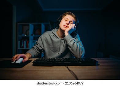 A Sleepy Gamer Sleeps At The Computer And Falls Asleep While Bored Playing In A Dark Room At Home.