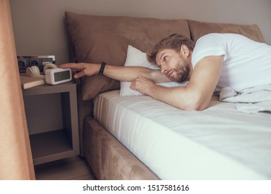 Sleepy male turning off his alarm clock after waking up