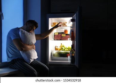 Sleepy Man With Pillow Near Refrigerator In Kitchen At Night