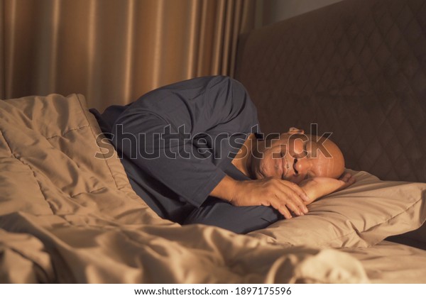 Sleepy old elderly black man yawning. African\
American people lying and sleeping on bed in bedroom at late night\
at home. Lifestyle