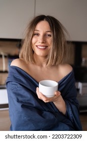 Sleepy Positive Woman Wrapped In Blue Bed Sheet Drinking Coffee In The Morning In The Kitchen