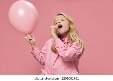 A Sleepy, Sad Girl Stands On A Pink Background With A Pink Balloon In Her Hand And Yawns