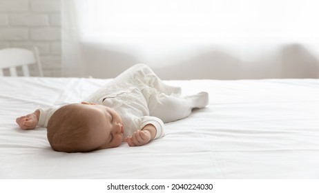 Sleepy silent few month infant resting in double bed with white sheet. Cute adorable peaceful baby in bodysuit sleeping in bedroom, lying on back on mattress. Childhood, child care, bedtime concept
