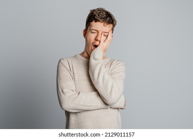 Sleepy Teenager Boy Bored Yawning Tired Covering Mouth With Hand, Standing Over Gray Background. Restless And Sleepiness