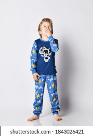 Sleepy and tired blond 5-6 y.o. kid boy in pyjamas with african animals pattern and map print stands and yawns covering his mouth with hand, is getting ready for bed, going to sleep.