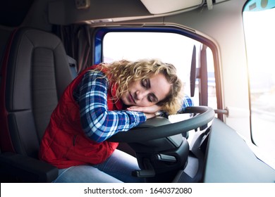 Sleepy and tired female truck driver sleeping over steering wheel inside truck vehicle cabin. People working overtime.