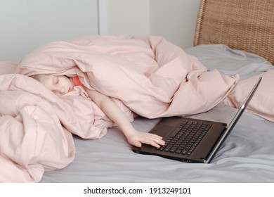 Sleepy Tired Girl Lying In Bed Under Blanket And Learning In Virtual Online School Class. Kid Working On Laptop Internet At Home. Child Using Wireless Technology Education. Homeschooling For Children.