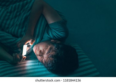 Sleepy tired teenage man under the blanket using smartphone with white screen at late night, can not sleep/ Insomnia, nomophobia, sleep disorder concept/ Dependency on a cell phone, hard lighting. - Powered by Shutterstock