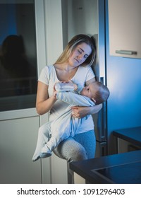 Sleepy Tired Woman Feeding Her Baby Boy On Kitchen At Night