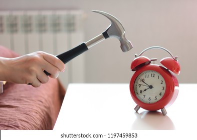 Sleepy Woman In The Bed Is Trying To Smash A Red Alarm Clock By Hammer In Her Hand. Kill The Alarm Clock Concept.