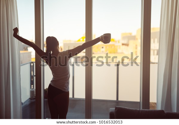 Sleepy woman stretching,drinking a coffee to wake\
up early in the monday morning sunrise.Starting your\
day.Wellbeing.Positive energy,productivity,happiness,enjoyment\
concept.Morning ritual