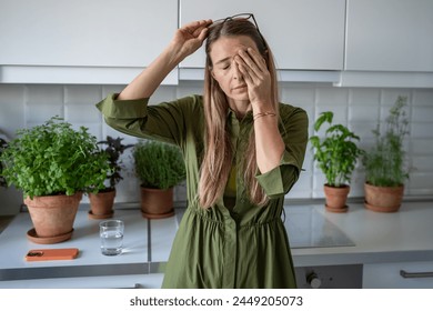 Sleepy woman suffering from chronic fatigue rubbing eyes on kitchen at home. Tired middle aged female feeling bad from lack of rest, headache, lack of energy after party, sleepless night. 