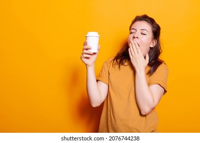 Sleepy Woman Yawning While Holding Cup Of Hot Coffee On Camera. Young Person Feeling Exhausted And Falling Asleep While Drinking Beverage With Caffeine To Stay Awake And Have Energy.