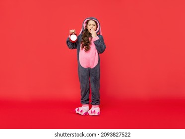 Sleepy Yawning Teen Girl In Soft Night Suit Hold Alarm Clock On Red Background, Early Morning