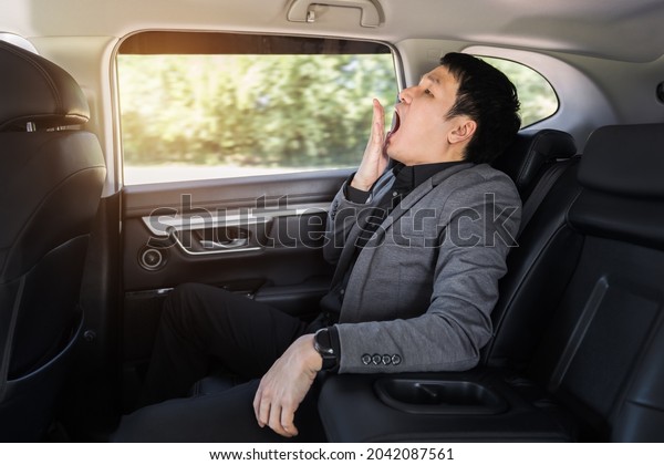sleepy young business man yawning while sitting in the\
back seat of car 