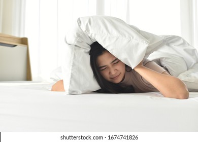 Sleepy  young woman sleeping on the bed use the pillow to close the ears while the alarm clock in morning.