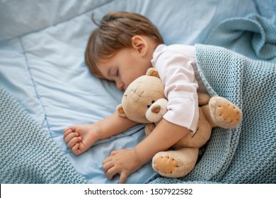 Sleepyhead. Young boy peacefully sleeping on a blue pillow. Baby needs his sleep! Baby boy sleeping with teddy bear and pacifier. Baby sleeping covered with soft blanket  - Powered by Shutterstock