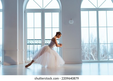 Slender Ballerina In Long White Tulle Skirt, Crouching In Bow Pose, Against Backdrop Of Huge Window