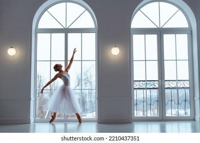 Slender Ballerina In Long White Tulle Skirt, Crouching In Bow Pose, Against Backdrop Of Huge Window