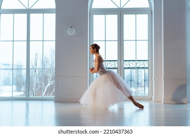 Slender Ballerina In Long White Tulle Skirt, Crouching In Bow Pose, Against Backdrop Of Huge Window