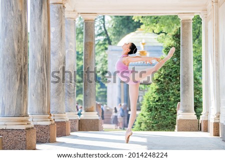 Slender ballerina in pointe shoes and wearing silhouette costume dancing against the background of antique architecture in the park