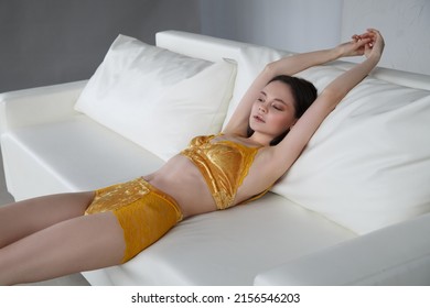 Slender Beautiful Brunette Girl In Yellow Velvet Lingerie Resting On A White Sofa.